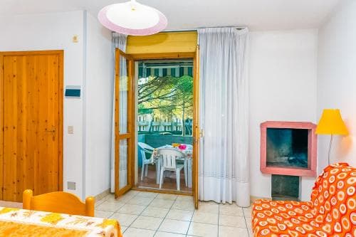 A cozy apartment interior with tiled floors, wooden accents, and a bright doorway leading to a tree-lined patio, perfect for travelers seeking a comfortable and inviting stay in a serene environment.