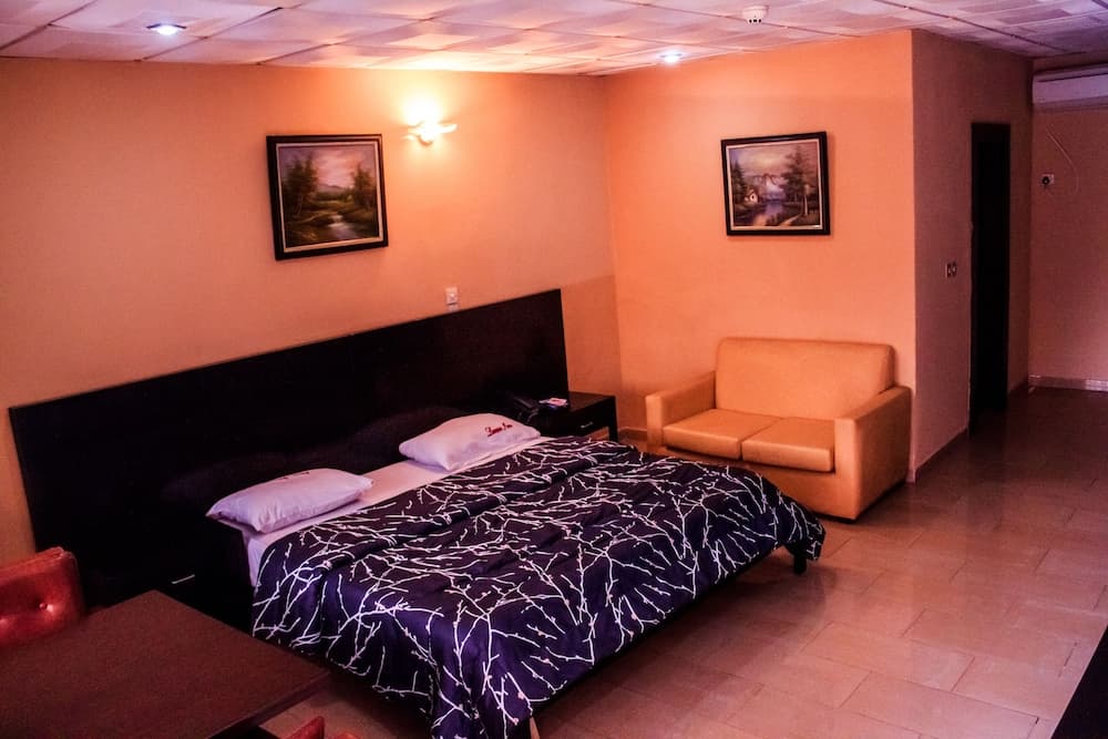 A cozy hotel room with warm-toned walls, framed landscape paintings, a comfortable bed with a patterned duvet, and a plush armchair, ideal for travelers seeking relaxation and comfort.