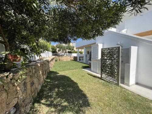 A serene Mediterranean villa garden with lush greenery, stone walls, and modern white architecture offers a tranquil retreat for vacationers seeking relaxation.