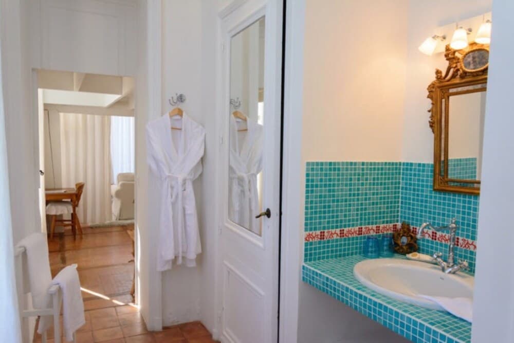 A cozy bathroom with turquoise mosaic tiles, a white robe hanging on the wall, and a vintage mirror exudes a serene and inviting atmosphere, perfect for travelers seeking relaxation in a charming accommodation.