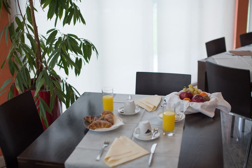 A cozy breakfast nook features a neatly set table with croissants, fruit, orange juice, and coffee, surrounded by modern chairs and a lush indoor plant, ideal for travelers seeking a serene morning start in a hotel dining area.