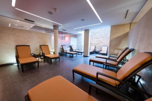 A serene indoor relaxation area features orange lounge chairs arranged on polished floors under modern lighting, ideal for travelers seeking a tranquil spa retreat.