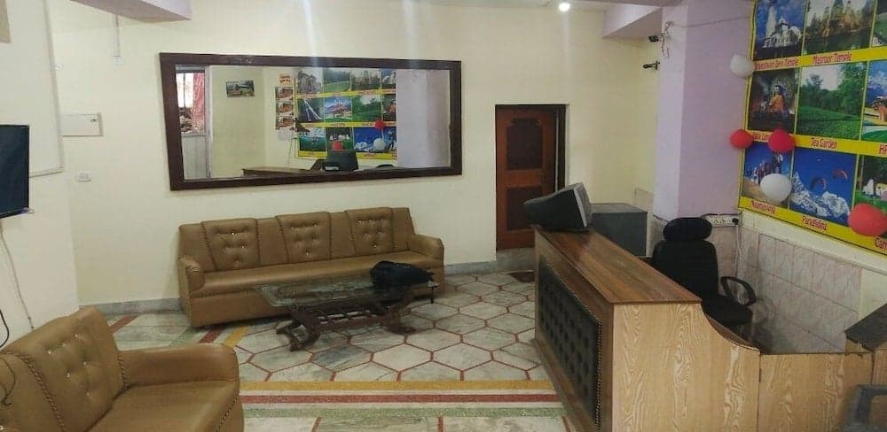 A cozy hotel lobby features a brown leather sofa set against a tiled floor, a reception desk adorned with colorful travel posters, and a large mirror reflecting the inviting atmosphere, ideal for travelers seeking comfort and information.