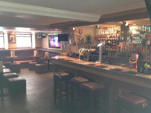 A cozy pub interior features plush leather booths by the window, a well-stocked bar with stools, and a relaxed atmosphere ideal for travelers seeking a casual drink or social gathering spot.