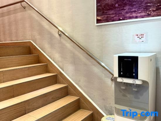 A modern staircase with wooden steps ascends beside a sleek water dispenser in a clean, well-lit indoor space, ideal for travelers seeking refreshment during transit or accommodation stays.