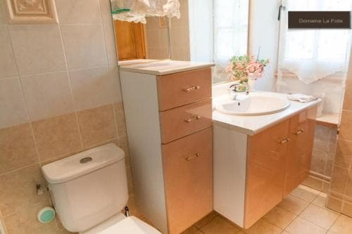 A cozy bathroom with beige tiles, wooden cabinets, a sink adorned with flowers, and a toilet, ideal for travelers seeking comfort in a quaint accommodation setting.