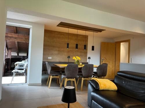 A cozy modern apartment features a sleek dining area with wooden accents, comfortable seating, and a bright, inviting atmosphere perfect for travelers seeking a stylish yet homey retreat.