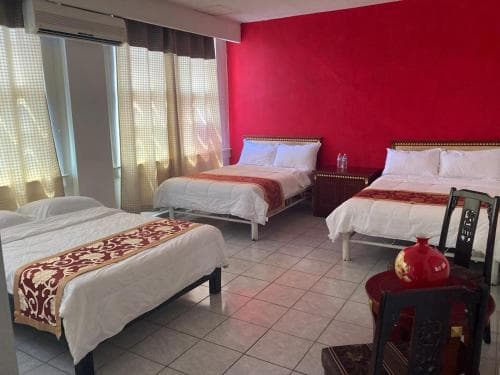 A cozy hotel room with three neatly arranged beds, a vibrant red accent wall, and traditional decor creates a welcoming atmosphere ideal for family travelers seeking comfort and style.
