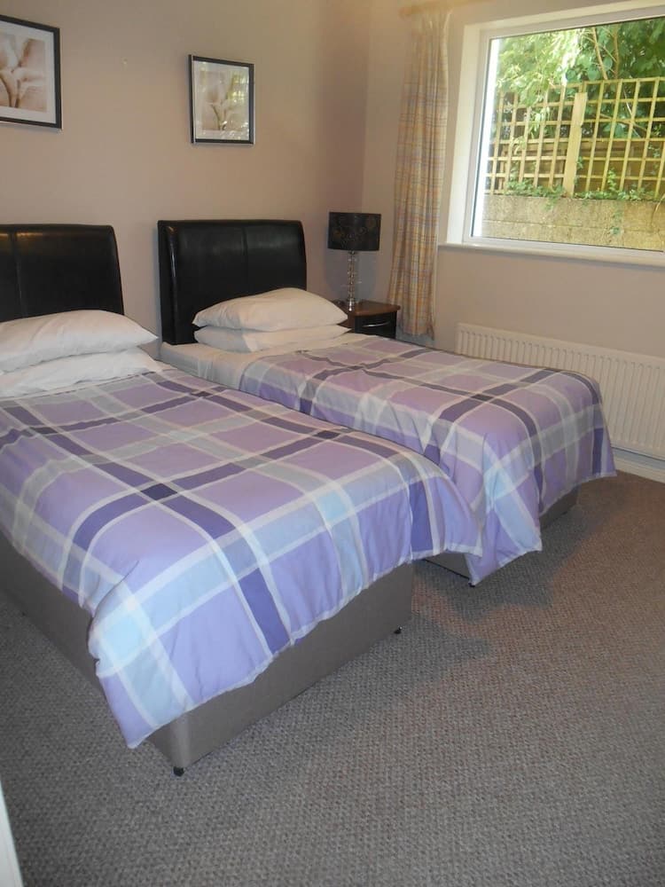 A cozy twin-bedded room with purple plaid bedding, framed artwork, and a window view of greenery, ideal for travelers seeking a comfortable and serene accommodation.
