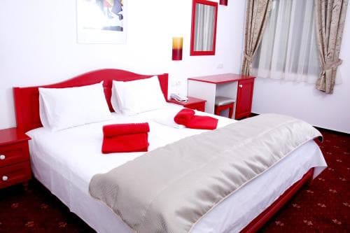 A cozy hotel room features a neatly made bed with red accents, a small desk, and soft lighting, creating a welcoming atmosphere ideal for travelers seeking comfort and relaxation.