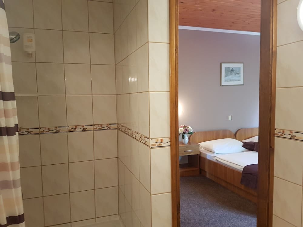 A cozy hotel room with wooden accents and a neatly made bed is viewed through an open door from a tiled bathroom, ideal for travelers seeking comfort and convenience.
