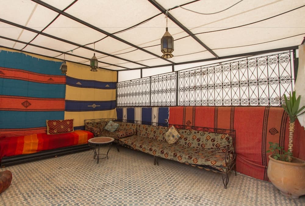 A cozy tented lounge with vibrant tapestries, patterned sofas, and hanging lanterns offers a serene retreat for travelers seeking cultural immersion in a desert oasis setting.