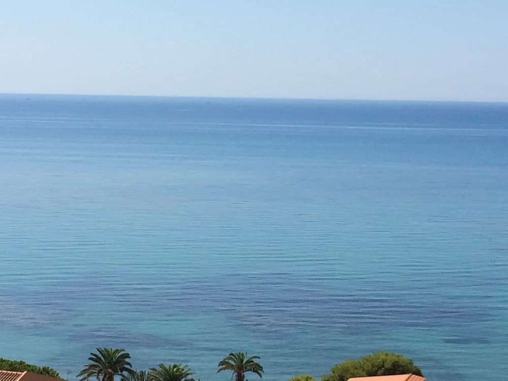 A serene coastal scene with calm turquoise waters, palm trees, and terracotta rooftops under a clear blue sky, ideal for relaxing beachside vacations.