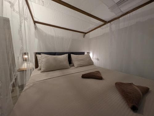 A cozy bedroom with a neatly made bed under a mosquito net canopy, featuring soft lighting and folded towels, evokes a serene and inviting atmosphere ideal for travelers seeking comfort in tropical destinations.
