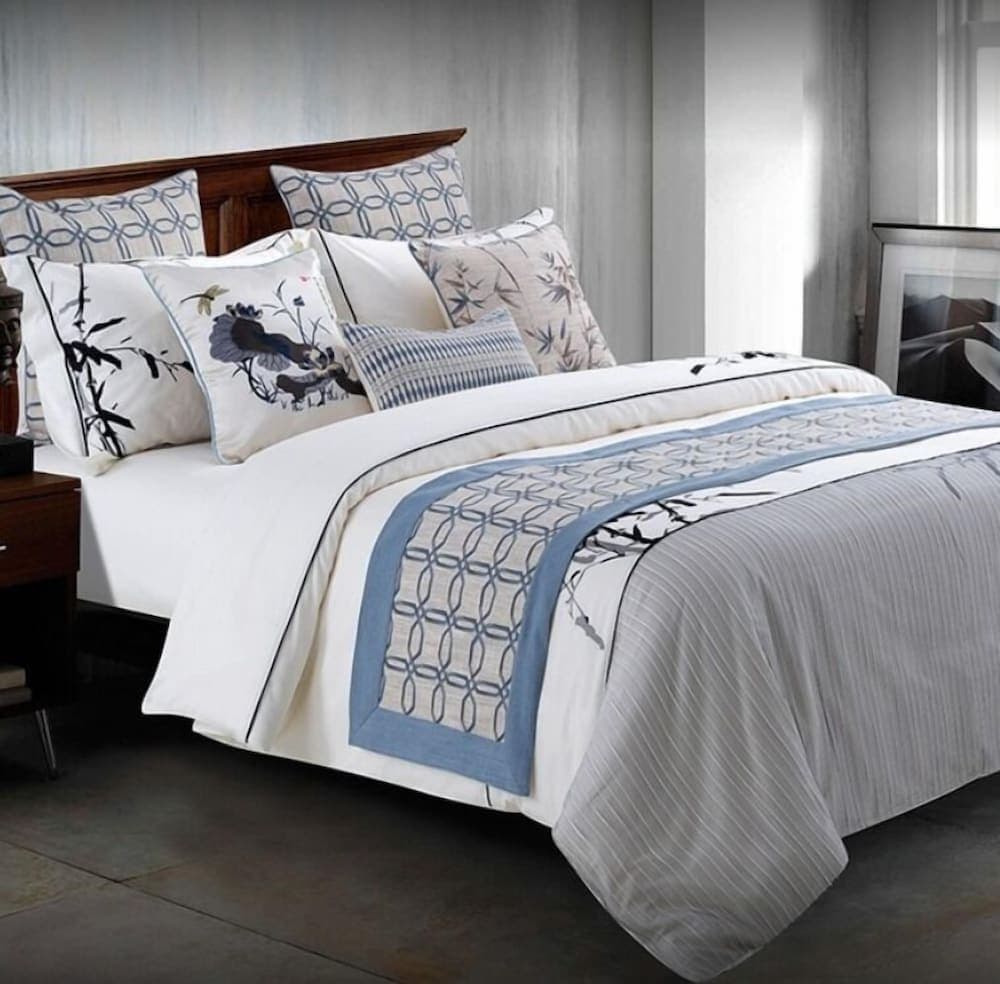 A serene bedroom scene features a neatly arranged bed with elegant blue and white bedding adorned with bamboo motifs, ideal for travelers seeking a tranquil and stylish accommodation experience.