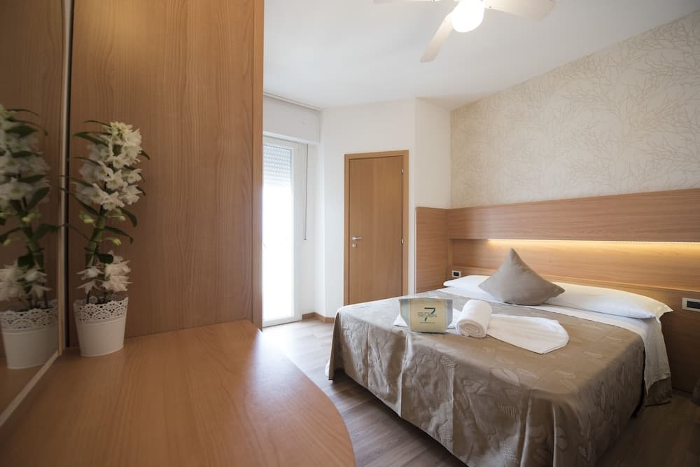 A cozy hotel room with a neatly made bed, wooden furnishings, soft lighting, and decorative flowers creates a welcoming atmosphere ideal for travelers seeking comfort and relaxation.