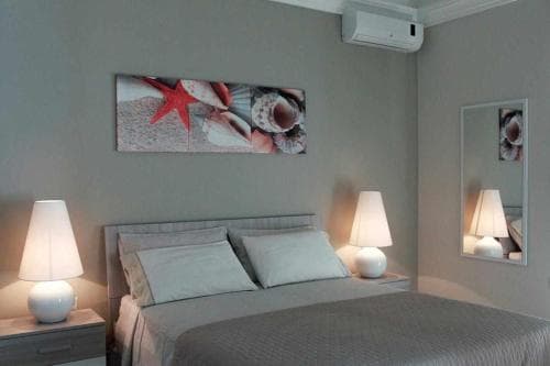 A cozy hotel bedroom features a neatly made bed flanked by two bedside lamps under soft lighting, adorned with a seaside-themed wall art, creating a serene and inviting atmosphere ideal for travelers seeking relaxation.
