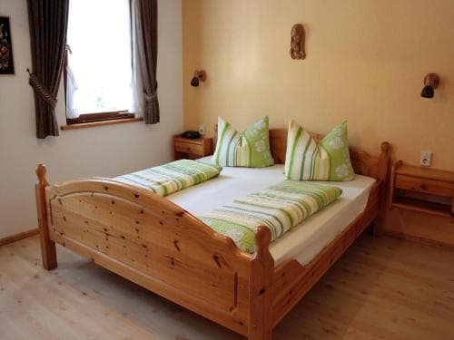 A cozy bedroom with a rustic wooden bed adorned in green and white bedding, featuring warm lighting and wooden furnishings, ideal for travelers seeking a serene and inviting accommodation experience.