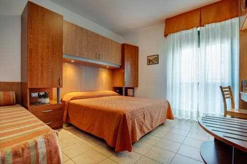 A cozy hotel room features warm-toned furnishings, a neatly made bed, and a bright window with sheer curtains, creating an inviting atmosphere ideal for travelers seeking comfort and relaxation.