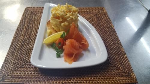 A beautifully plated dish featuring scrambled eggs, smoked salmon, and garnishes sits on a woven placemat in a modern dining setting, ideal for travelers seeking a gourmet breakfast experience.