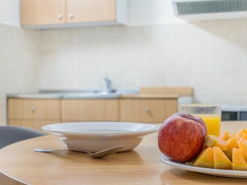 A cozy kitchen scene featuring a wooden table set with fresh fruit and juice, evoking a warm, inviting atmosphere ideal for travelers seeking a comfortable self-catering accommodation.
