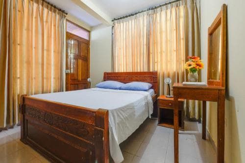 A cozy bedroom with wooden furniture, floral curtains, and a vibrant flower arrangement creates a warm and inviting atmosphere, ideal for travelers seeking comfort in a budget-friendly accommodation.