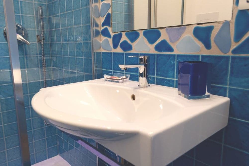 A serene hotel bathroom features a modern white sink against vibrant blue tiled walls, complemented by a decorative mosaic mirror and sleek fixtures, ideal for travelers seeking comfort and style.