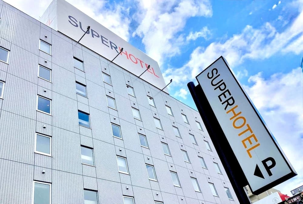 A modern SuperHotel building with a prominent sign stands under a vibrant blue sky, ideal for travelers seeking budget-friendly accommodations in an urban setting.