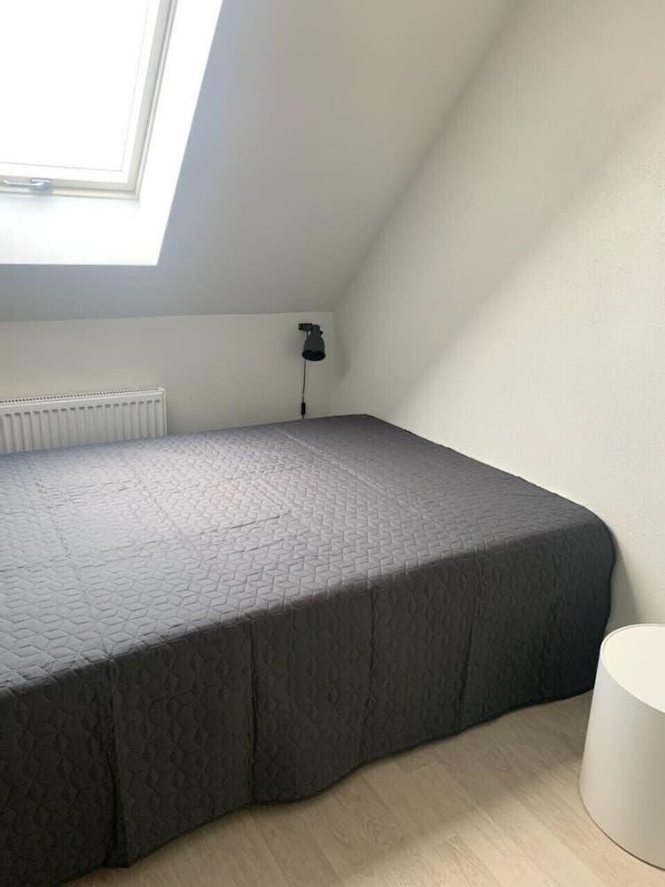 A cozy attic bedroom with a neatly made bed under a skylight, featuring minimalist decor and soft lighting, ideal for travelers seeking a serene and intimate retreat.