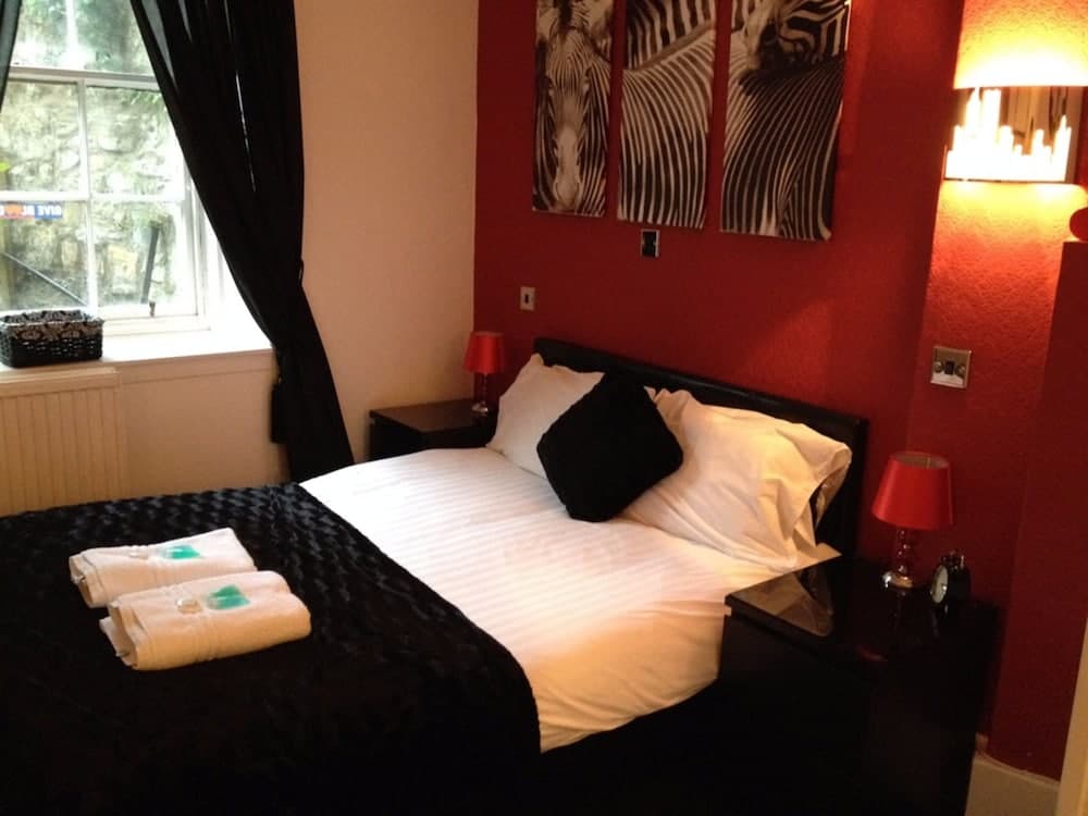 A cozy hotel room features a neatly made bed with white linens and black accents, red walls adorned with zebra artwork, and a window view of greenery, ideal for travelers seeking comfort and style.