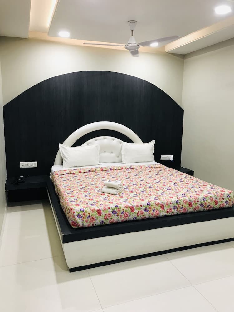 A cozy hotel room features a modern bed with a floral comforter against a sleek black headboard, set in a minimalist space ideal for travelers seeking comfort and style.