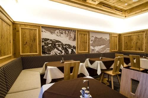 A cozy mountain-themed restaurant with wooden interiors, snowy mountain murals, and neatly set tables invites travelers to enjoy a warm dining experience in an alpine setting.