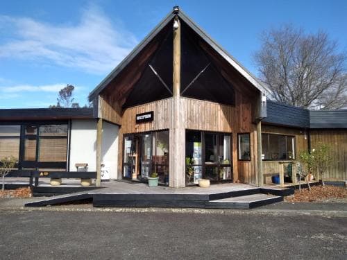 A cozy wooden café with a modern design stands invitingly under a clear blue sky, surrounded by leafless trees and mulched landscaping, perfect for travelers seeking a serene spot to relax and enjoy refreshments.