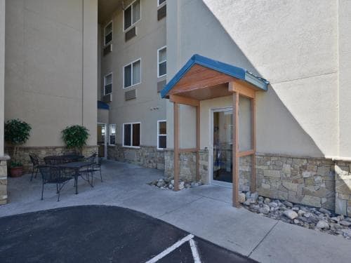 A cozy outdoor seating area beside a hotel entrance features a wooden gazebo, stone walls, and potted plants, creating a welcoming atmosphere ideal for travelers seeking relaxation or a quiet moment during their stay.