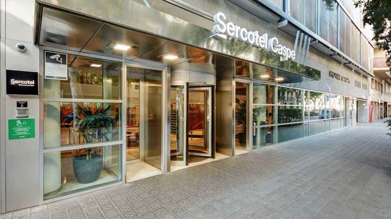 The modern facade of Sercotel Caspe in Barcelona's Eixample district features sleek glass doors and inviting greenery, creating a welcoming urban atmosphere ideal for travelers seeking a stylish city stay.