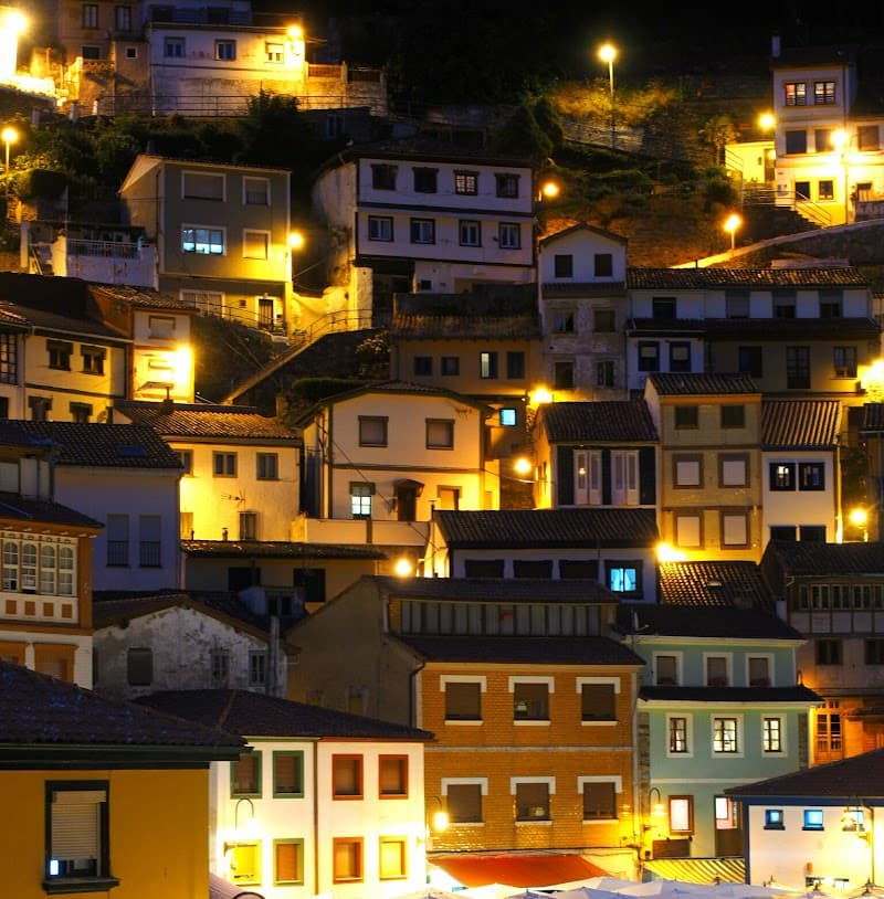 A cozy evening scene in a hillside village with warmly lit, colorful houses nestled together, ideal for travelers seeking a charming and atmospheric European getaway.