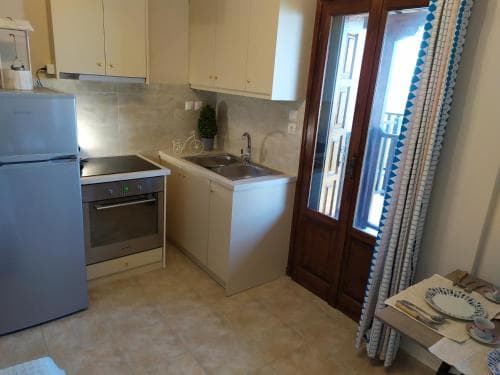 A cozy kitchen with white cabinets, stainless steel appliances, and a tiled floor opens to a balcony through wooden doors, ideal for travelers seeking a homey and functional space for self-catering stays.