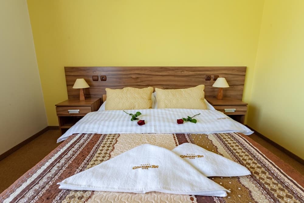 A cozy hotel room with vibrant yellow walls, wooden furnishings, neatly arranged towels, and red roses on the bed evokes a warm and inviting atmosphere ideal for travelers seeking comfort and relaxation.
