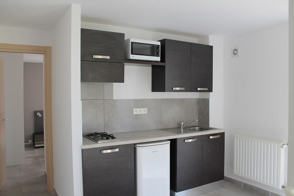 A modern, minimalist kitchenette with sleek gray cabinets, a compact refrigerator, and a microwave offers a cozy and functional space ideal for travelers seeking self-catering accommodations.