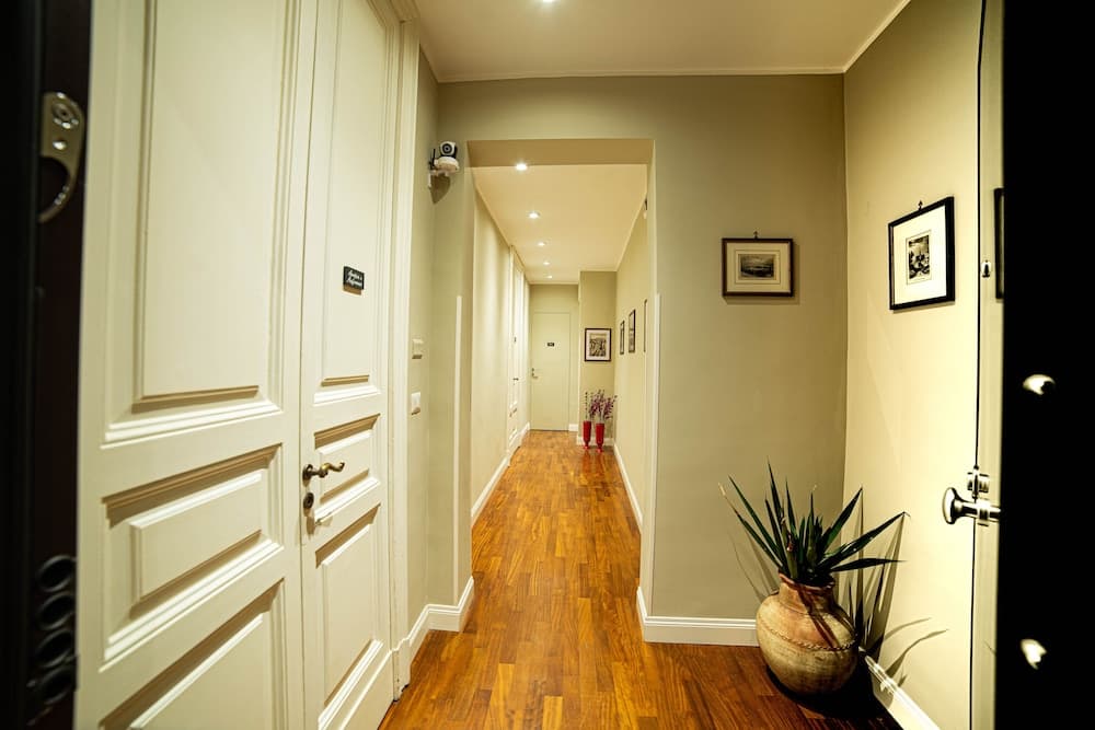 A warmly lit residential hallway with wooden flooring, cream-colored walls adorned with framed artwork, and a decorative potted plant creates an inviting atmosphere ideal for showcasing home interiors in real estate listings.