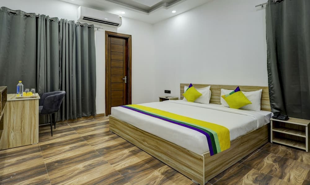 A cozy hotel room with wooden flooring, vibrant bedding, and modern amenities offers a comfortable stay for travelers seeking relaxation.