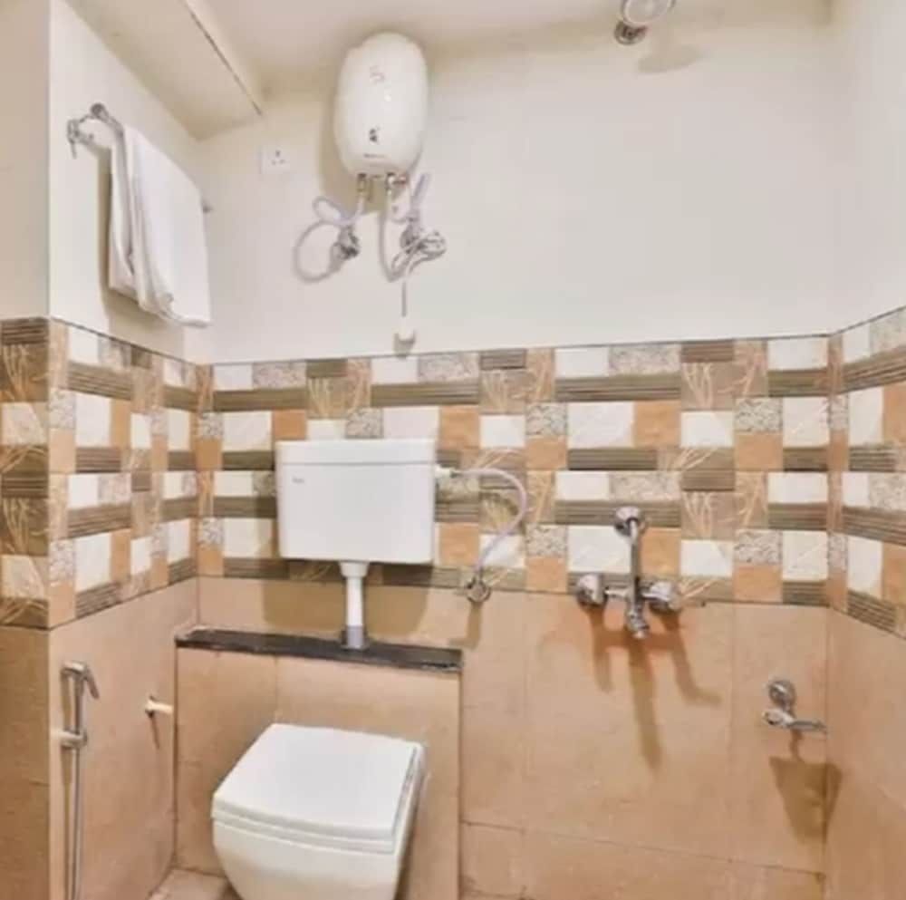 A cozy bathroom with beige and patterned tiles features a toilet, wall-mounted water heater, and taps, ideal for travelers seeking comfortable accommodations.