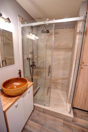 A modern bathroom with a sleek glass-enclosed shower, wooden vanity, and stylish sink offers a cozy and inviting space ideal for travelers seeking comfort in their accommodations.