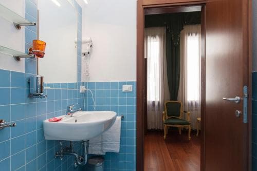 A cozy hotel bathroom with blue tiled walls and a sink leads to a warmly lit room with wooden floors, inviting travelers seeking comfort and convenience.