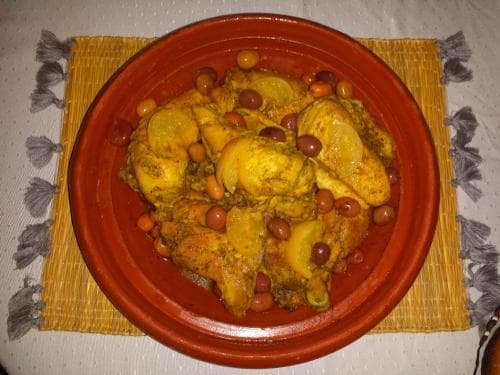 A vibrant Moroccan tajine dish featuring chicken, olives, and spices served on a terracotta plate atop a woven mat, evoking warmth and culinary adventure for food enthusiasts exploring global cuisine.