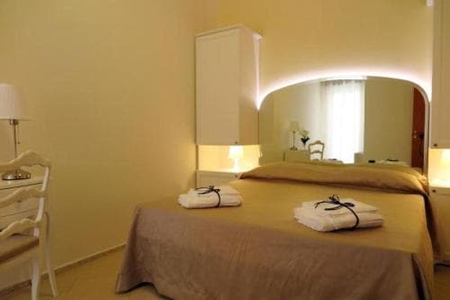 A cozy hotel room features a neatly made bed with folded towels, soft lighting from bedside lamps, and a large mirror reflecting the serene ambiance, ideal for travelers seeking comfort and relaxation.