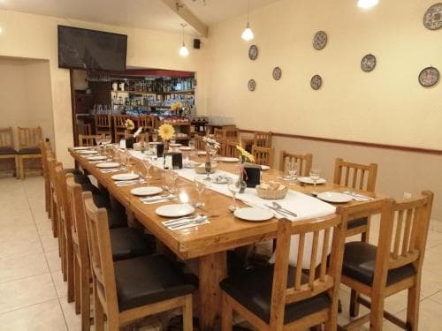 A cozy restaurant dining area features wooden tables set for a meal, adorned with decorative plates on the walls and a well-stocked bar in the background, ideal for travelers seeking a warm and inviting spot to enjoy local cuisine.