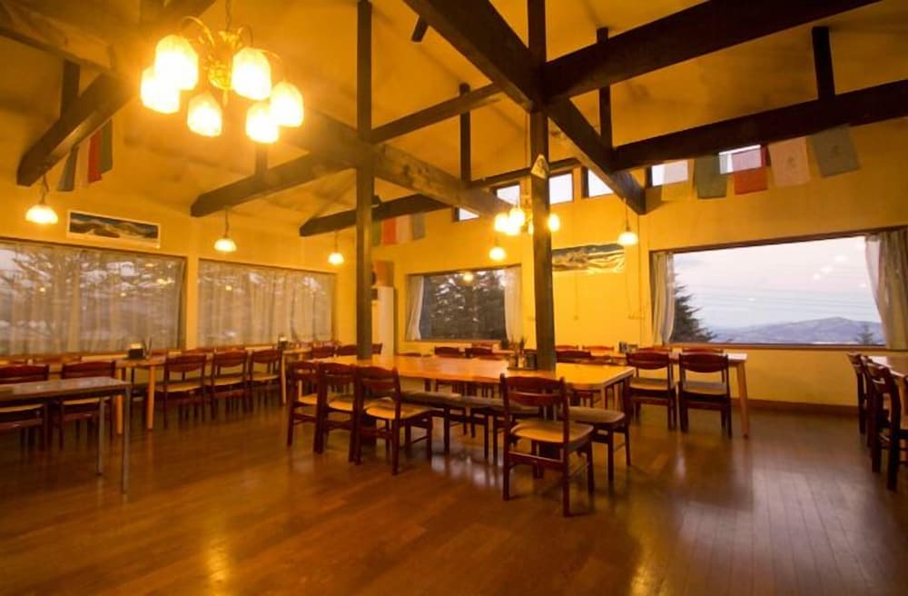 A cozy, rustic dining hall with wooden beams, warm lighting, and large windows offering scenic mountain views, ideal for travelers seeking a serene retreat experience.