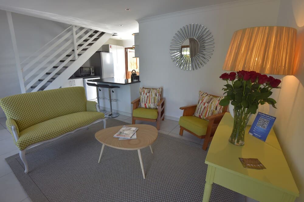 A cozy living space with vibrant green furniture, a sunburst mirror, and red roses creates an inviting atmosphere ideal for travelers seeking comfort in a modern apartment setting.