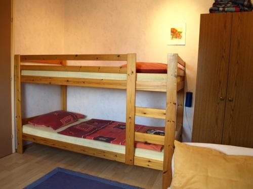 A cozy hostel room features wooden bunk beds with red bedding, a warm ambiance, and simple decor, ideal for budget travelers seeking comfortable accommodation.